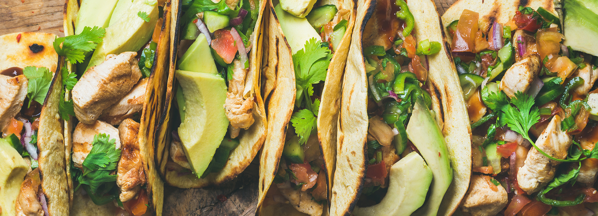 Close-up shot of six open-faced
                    chicken soft tacos with cilantro and avocado.